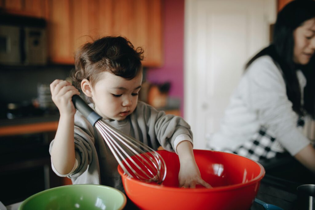 pexels-photo-7677938-7677938 Young child assisting in the kitchen with a large red mixing bowl, showcasing curiosity and bonding time.